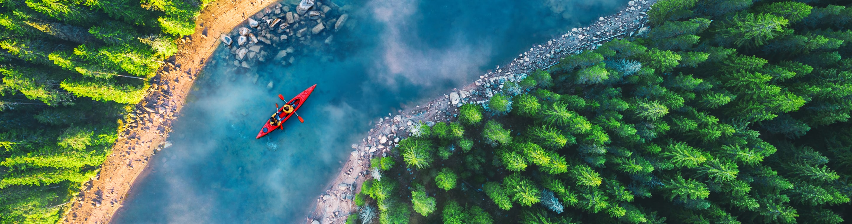 Red kayak traveling down blue river shot from above