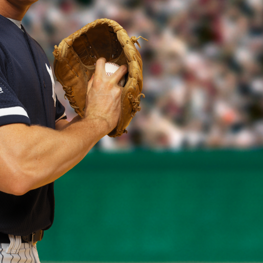 A baseball player wearing a dark blue jersey with white stripes on the sleeves and holding a brown baseball glove is preparing to catch a ball.